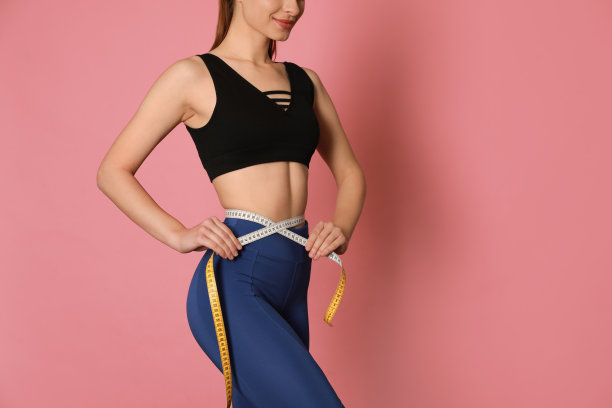 快乐的女人在运动服测量腰部与胶带在粉红色的背景，特写。空间的文本图片下载