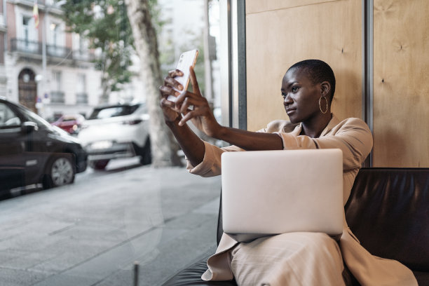 快乐的非裔美国年轻女子坐在自助餐厅，一边用笔记本电脑一边自拍图片下载
