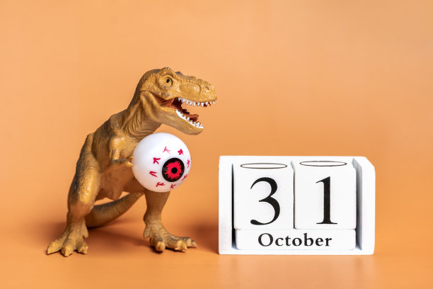 玩具恐龙暴龙在它的爪子里抱着眼睛，日历日期10月31日孤立在橙色背景节日贺卡万圣节快乐的创意最小的概念图片下载
