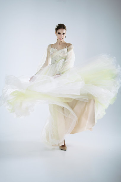 在照相馆里，年轻的女孩模特穿着婚纱，摆出动态地抬起腿和手臂的姿势图片下载