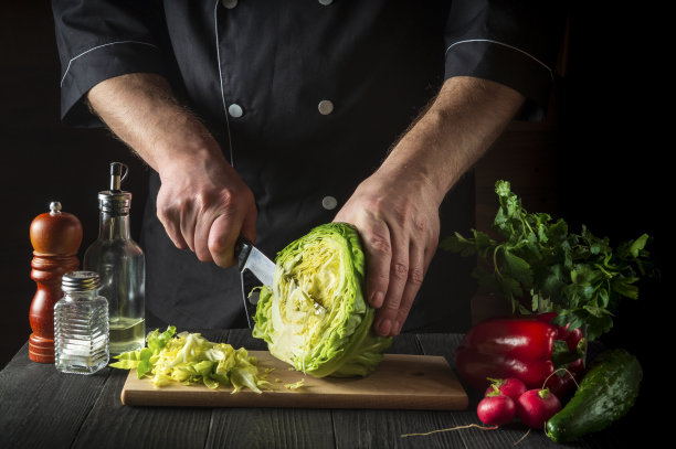 厨师用刀切新鲜的卷心菜沙拉在一个古老的厨房桌子上与新鲜的蔬菜。烹饪和餐厅或咖啡馆的概念图片下载