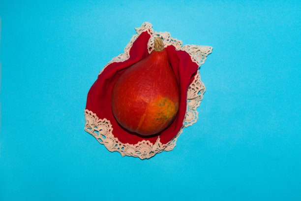 红色的橙色南瓜放在皱巴巴的桌布上，蓝色的背景图片下载