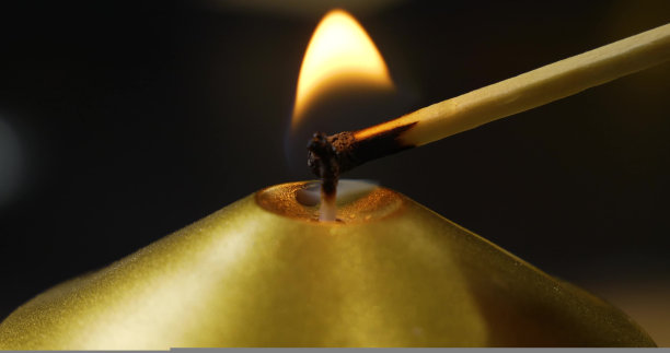 在黑色背景上，一根火柴点燃了金色蜡烛的灯芯。漂亮的特写照片。概念背景和壁纸。图片下载