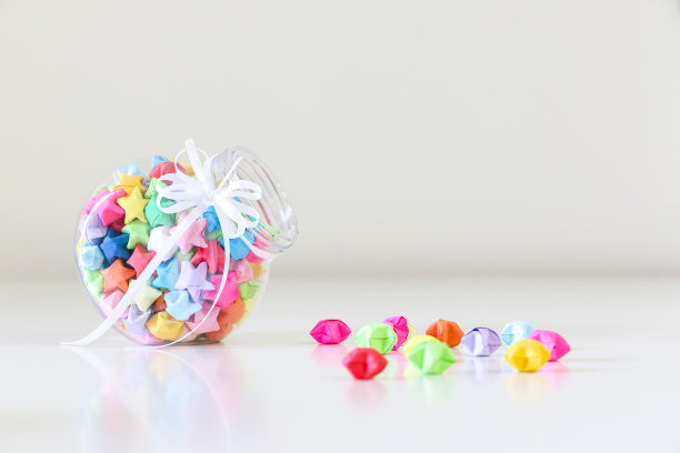 一罐手工制作的彩色折纸幸运星散落在白色的桌子上。幸运的星星代表爱和幸运的礼物。图片下载