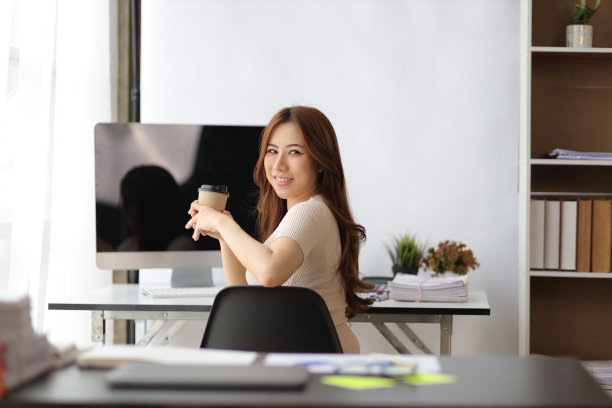 肖像的亚洲妇女在家庭办公室的电脑上工作，回头看相机。图片下载