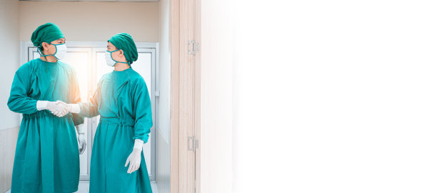 两名医生穿着防护消毒服，戴着手套、医用口罩，在医院走廊、走廊进行手术成功后握手。专业团队的外科医生。医疗、医院应急的概念图片下载