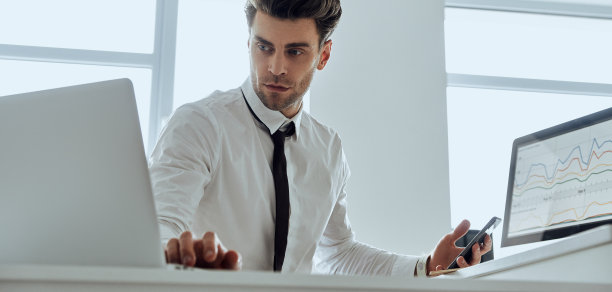 专注的年轻人坐在办公室里用电脑，拿着智能手机图片下载