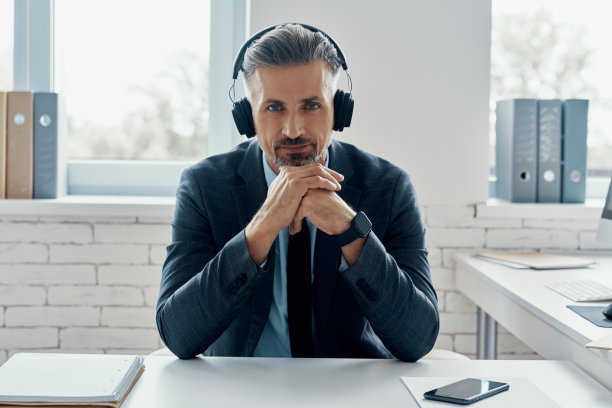 自信的商人戴着耳机坐在他的工作场所看着相机图片下载
