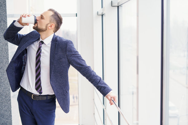一个穿着西装的年轻人正在喝热饮。图片下载