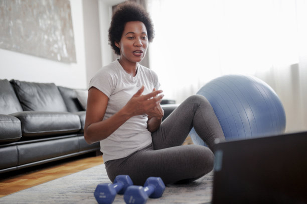 一位穿着运动服的女性坐在客厅的地板上用笔记本电脑。运动和娱乐的概念。图片下载