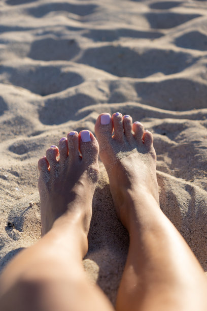 沙滩上沙滩上的腿和脚的特写，涂了指甲油的指甲和晒黑的腿。图片下载