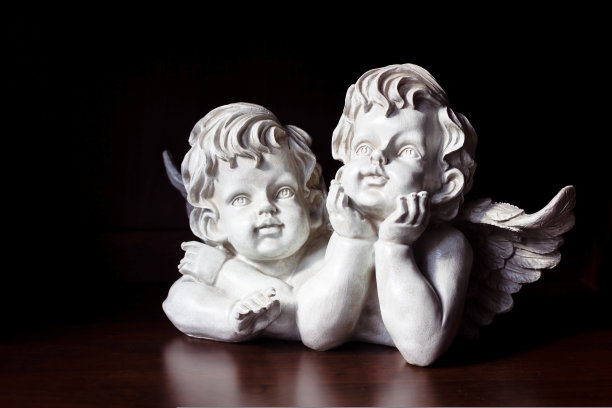 黑色背景上的白色天使。天使们双手托着脸，梦幻般地望着远方图片下载