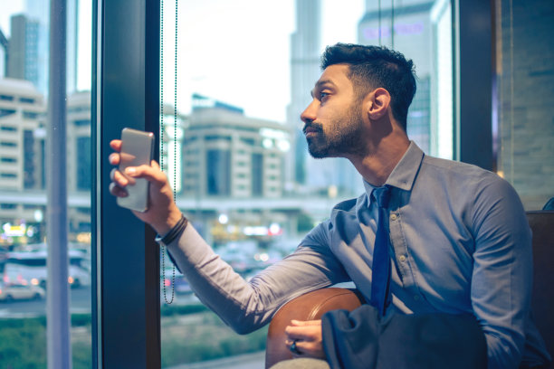 印度商人站在办公室窗户旁手持智能手机的侧面照图片下载