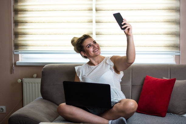 微笑的年轻女子自拍和使用笔记本电脑在家里图片下载