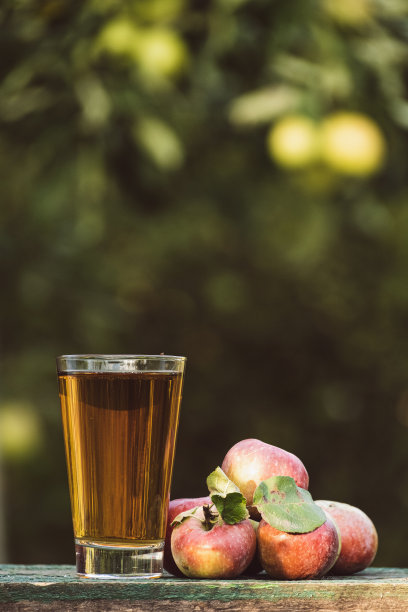 苹果汁放在花园里的木桌上，桌子周围都是苹果。农夫拿着一个罐子，把苹果园里的新鲜果汁倒进玻璃杯里。把苹果汁倒进玻璃杯里图片下载