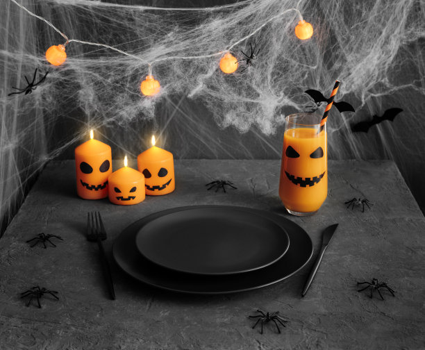 万圣节用黑色餐具的餐桌。节日的服务与燃烧的蜡烛和花环，南瓜汁，蜘蛛在深灰色的背景。空板。图片下载
