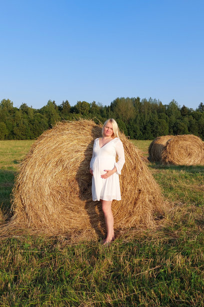 一位年轻的孕妇站在她的女儿旁边。干草堆附近。图片下载