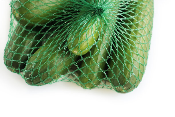 绿色的塑料网袋里装着一堆绿色的黄瓜。孤立在白色背景上。空间的文本。副本的空间。特写镜头。俯视图图片下载