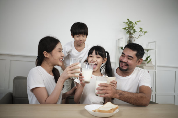 一个亚洲泰国家庭喝着新鲜的白牛奶和面包一起欢乐。图片下载