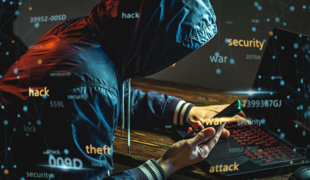 戴着兜帽、拿着手机的黑客正在一间黑暗的房间里用笔记本电脑键盘打字。网络犯罪、诈骗和身份盗窃图片下载