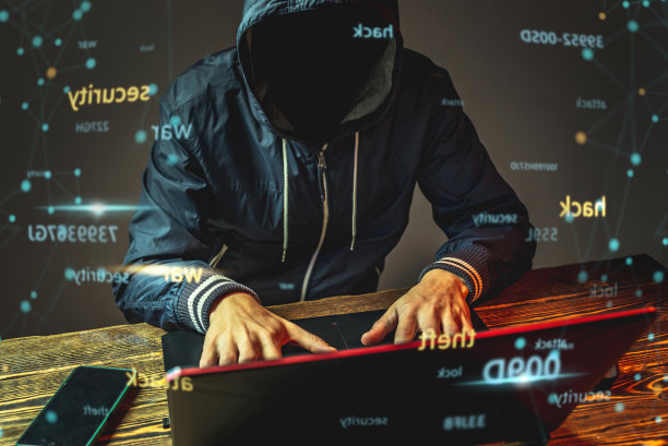 一个戴着兜帽的匿名黑客正在一间黑暗的房间里用笔记本电脑键盘打字。网络战争和Dos攻击的概念图片下载