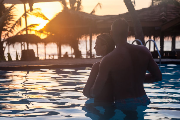 可爱的情侣剪影在游泳池，拥抱和看在日落背景。日落时分，男人和女人在游泳池里休息。夫妇享受蜜月。旅游度假的概念。本空间图片下载