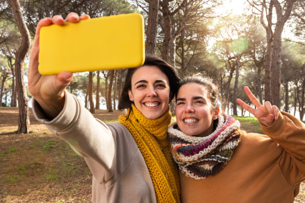 快乐的年轻女子在森林中散步时用手机自拍。图片下载
