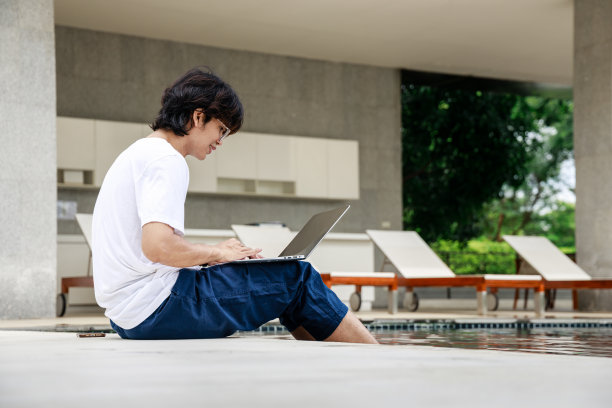 一个年轻人在游泳池边远程工作，把脚泡在水里，做自由职业者图片下载