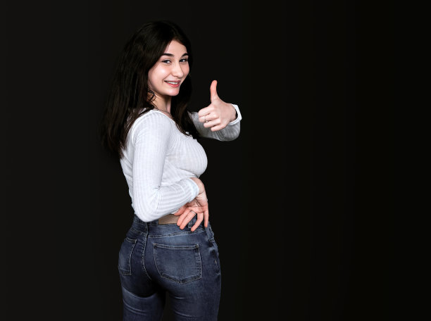 迷人的年轻棕色眼睛，身穿白色衬衫，站在半转姿势，拇指向上，微笑着看着镜头在黑色背景。横幅，放置文本的地方。图片下载