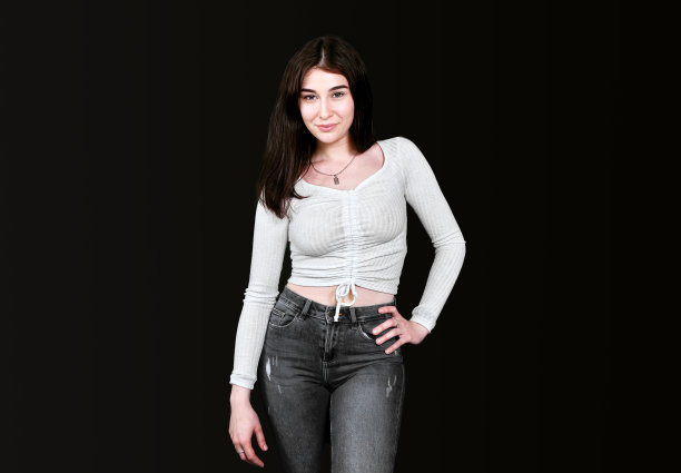 身材苗条的年轻女子身穿白色衬衫，胸部丰满，黑色牛仔裤，一只手放在腰上，站在黑色背景上微笑着看着镜头。横幅，放置文本的地方。图片下载