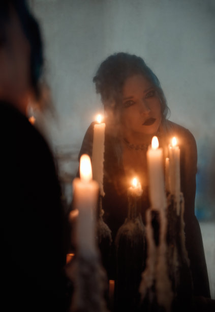 室内蜡烛中悲伤的哥特女孩的肖像。蓝色头发的哥特式女人看着旧的肮脏的镜子。年轻的女巫。复古风格图片下载