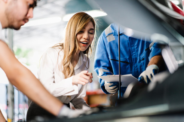 亚洲女性顾客一边观看发动机，一边向汽车机械师讲解和展示汽车零件的维修点，汽车服务和维护的概念图片下载