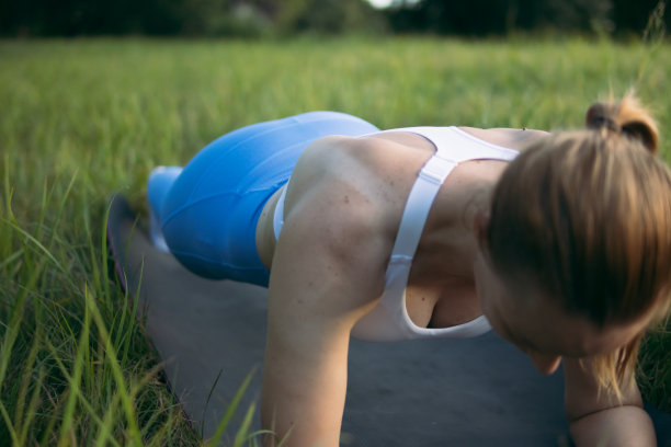 一个身材轻盈、体格健壮的姑娘，穿着蓝色的紧身裤和白色的衬裙，站在一块木板上。她喜欢在户外的灰色地毯上运动。健康生活方式的概念。高质量的照片图片下载