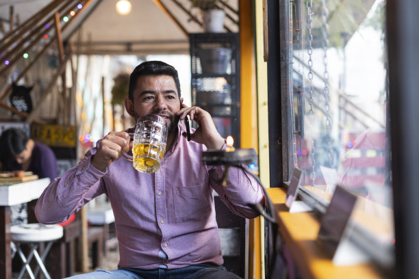 在一家餐馆里，拉丁裔的顾客在喝一杯啤酒的同时，由一位服务员为他服务图片下载