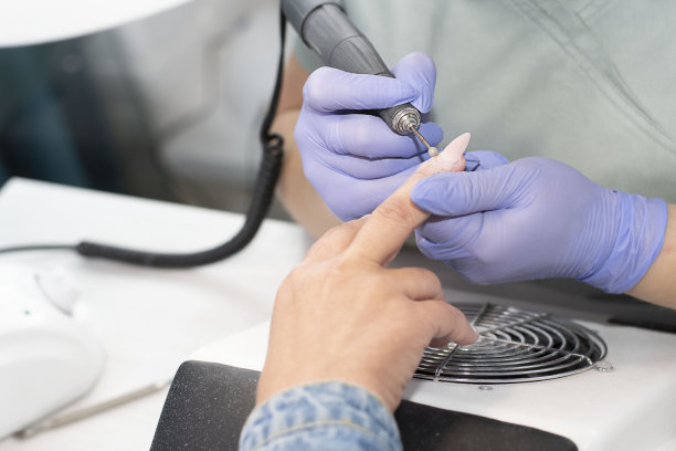 戴着淡紫色乳胶手套的美甲师在美容院为一位顾客去除黄色凝胶指甲油图片下载