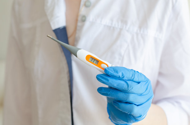 一名戴着防护手套的医务人员手持电子体温计。医生给病人量体温。增加体温。医疗设备。冠状病毒感染。图片下载