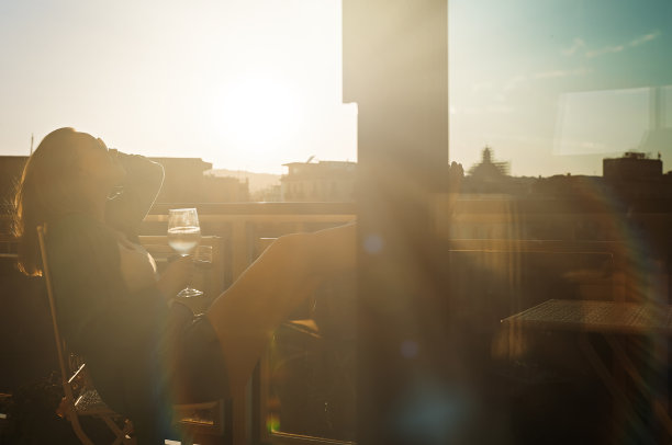 喝着白葡萄酒的女人在阳台上欣赏日落。图片下载