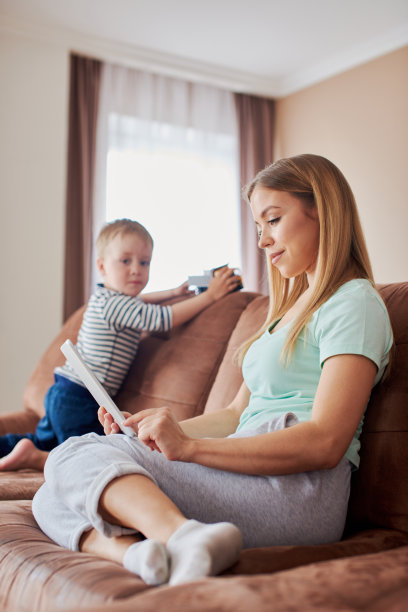 忙碌的母亲带着智能手机和平板电脑，她的儿子在她旁边玩图片下载