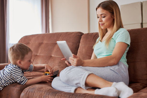 忙碌的母亲带着智能手机和平板电脑，她的儿子在她旁边玩图片下载