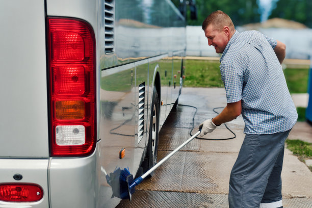 夏季，洗车工人在露天停车场用刷子手动清洗大型公共汽车。真正的工作流。图片下载