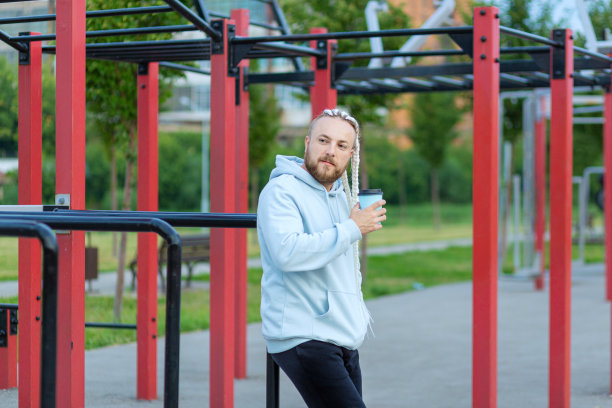 清晨，一名梳着辫子的男子在运动场喝咖啡。图片下载