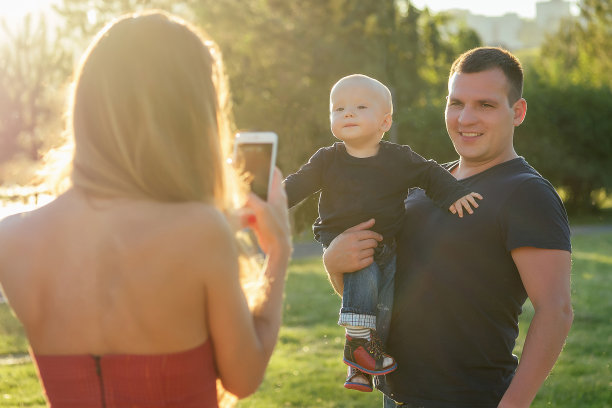 妈妈用手机拍下了公园里快乐的爸爸和抱着小宝宝的儿子图片下载