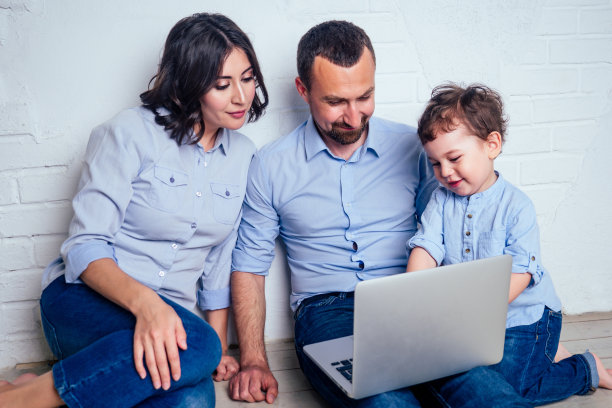 幸福的家庭美丽的母亲，小儿子和父亲玩开发儿童在线游戏在笔记本电脑在公寓的地板上坐图片下载