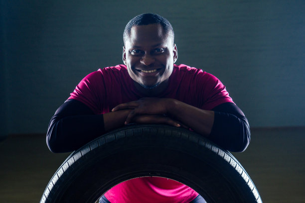 在健身房黑色背景工作室里用轮胎锻炼的肌肉发达的非洲裔美国青年男子图片下载