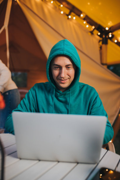 快乐的人自由职业者使用笔记本电脑在一个舒适的野营帐篷在一个夏天的晚上。户外度假度假的豪华露营帐篷。生活方式的概念图片下载