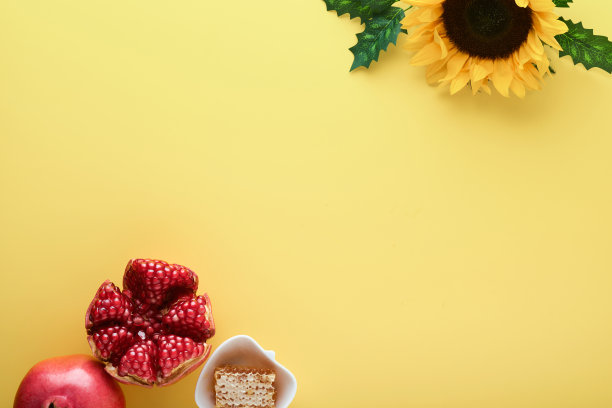 犹太新年。成熟的石榴，苹果，蜂蜜和向日葵，黄色的花在黄色的背景。组成与象征犹太人的犹太节日属性。带有复制空间的俯视图。图片下载