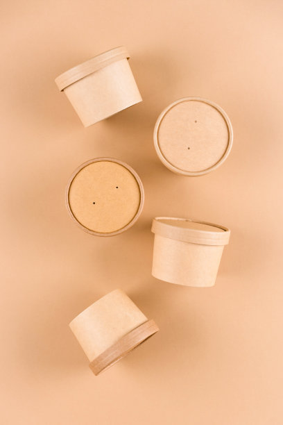 垂直构图与棕色纸食品容器汤或冰淇淋，杯与纸盖在浅棕色背景，模型图像。可持续的食品包装。单色图片下载