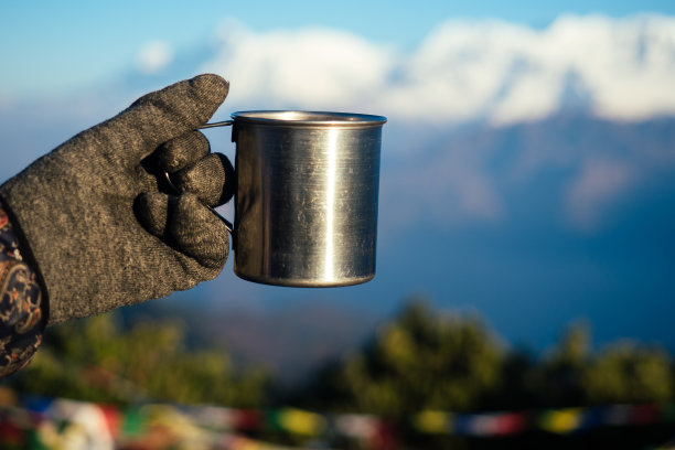 一个金属杯子，手里拿着一杯热饮，背景是群山。在山里积极度假的概念。在寒冷的季节旅游图片下载