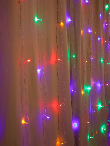 多色圣诞或新年花环的LED不同颜色的灯在米色棉窗帘在黑暗，家居装饰。垂直的照片。有选择性的重点。图片下载