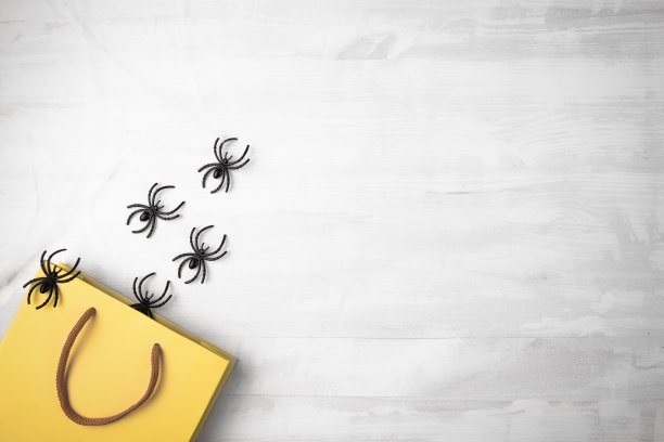 购物和万圣节礼物。黄色空白包装与黑色配给在白色木制背景与复制空间。图片下载